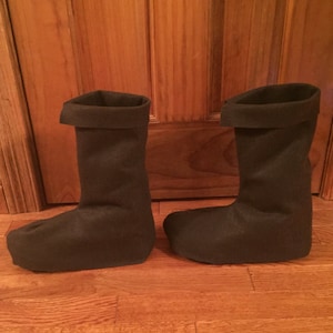 May include: A pair of black felt boots with a folded cuff. The boots are on a wooden floor.