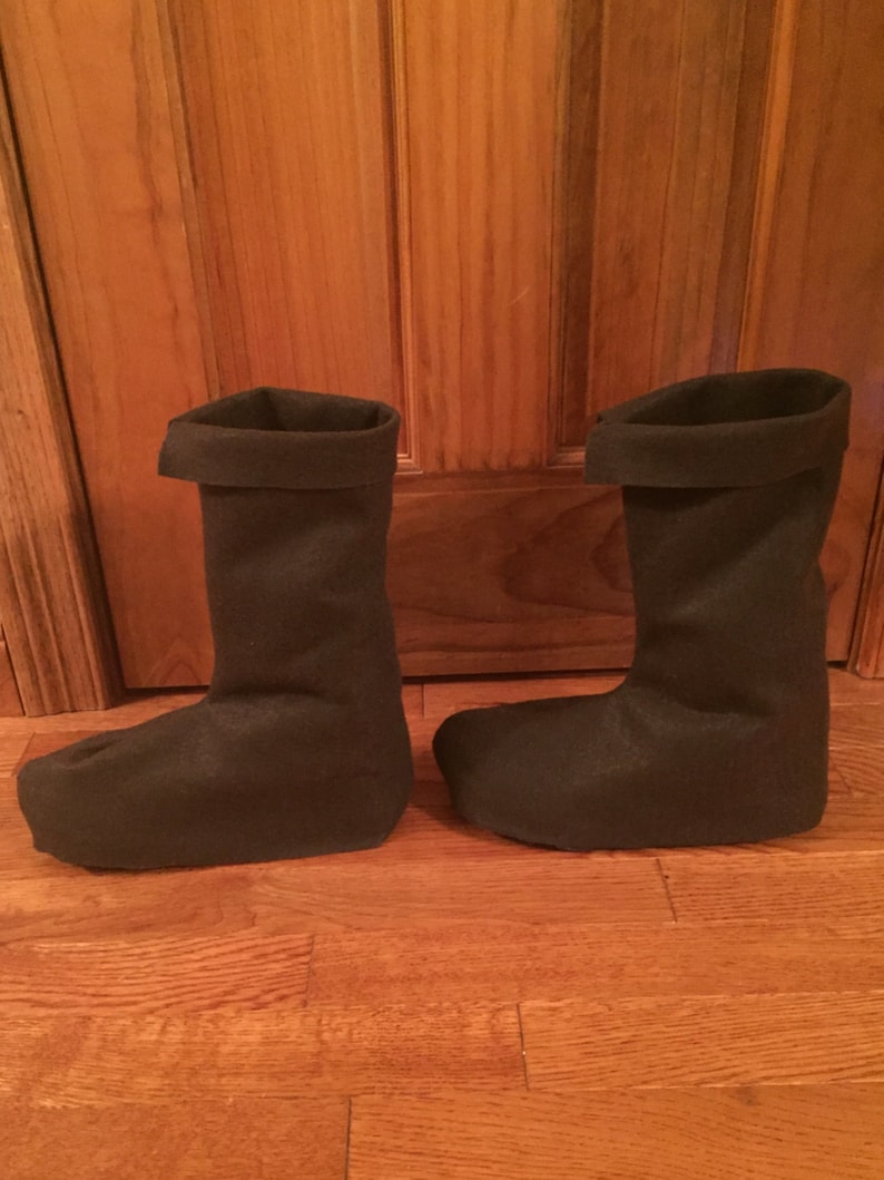 May include: A pair of black felt boots with a folded cuff. The boots are on a wooden floor.