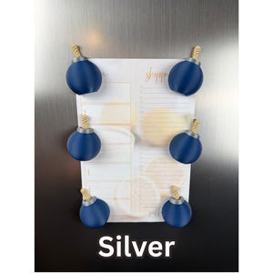 May include: Six dark blue spherical magnets with silver-coloured tops and tan rope-like fuses, arranged in pairs on a white shopping list notepad with orange text and citrus graphics. The word Silver is printed in white at the bottom of the image.