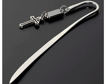 Könnte beinhalten: Silbernes Lesezeichen mit einem Kreuz-Anhänger. Das Lesezeichen ist dünn und hat ein gebogenes Ende. Der Kreuz-Anhänger ist detailliert und hat einen kleinen Ring daran.