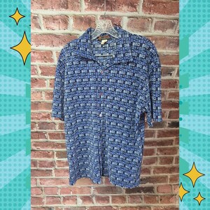 May include: A short-sleeve button-down shirt in shades of blue, black, and white. The fabric features a repeating geometric pattern of small squares and rectangles. The shirt has a standard collar and is displayed on a plastic hanger.