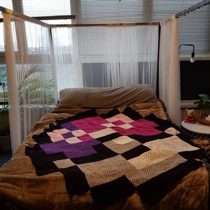 May include: A bed with a white canopy and a colorful crocheted blanket. The blanket is made of squares in pink, purple, black, and white.