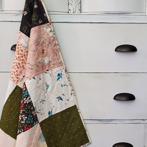 May include: A white dresser with six drawers and black metal handles. A patchwork quilt with various floral and geometric patterns is hanging on the top drawer.
