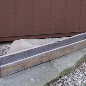 May include: A long, rectangular wooden planter box with a weathered gray finish. The planter is made of reclaimed wood and has a rustic look.