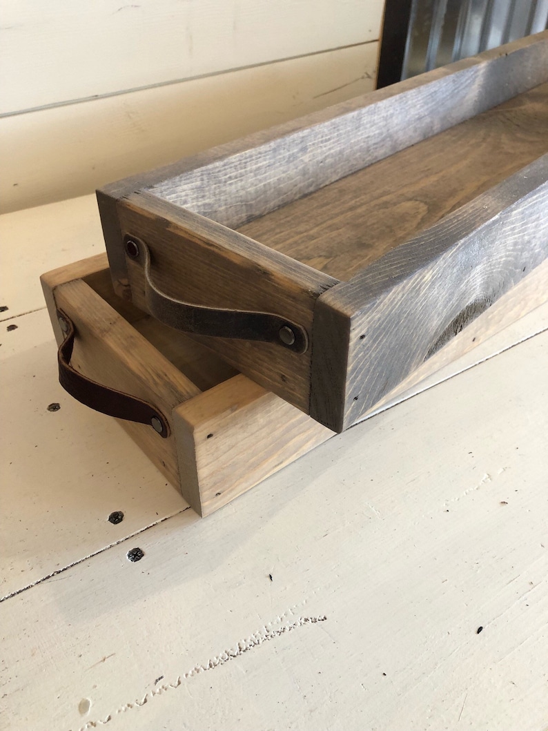 May include: Two wooden trays with leather handles. The trays are stacked on top of each other. The trays are made of reclaimed wood and have a rustic finish.