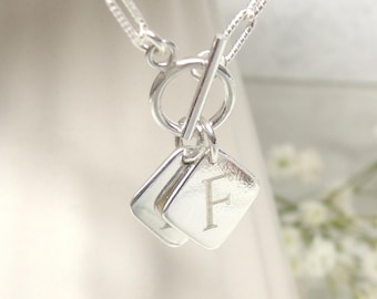 May include: Silver necklace with a toggle clasp and two square charms with the letter 'F' engraved on them.
