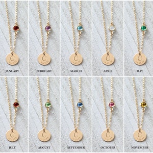 May include: Twelve gold necklaces with a small gemstone charm and a larger round charm with a letter 'C' and the date '09.21.18'. Each necklace represents a different month of the year with a corresponding birthstone: January (garnet), February (amethyst), March (aquamarine), April (diamond), May (emerald), June (pearl), July (ruby), August (peridot), September (sapphire), October (opal), November (topaz), and December (blue topaz).