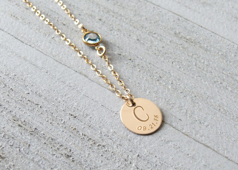 May include: Gold necklace with a small blue gemstone and a round pendant with the letter "C" and the date "09.21.18" engraved on it.