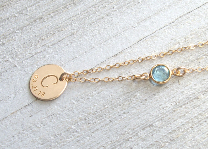May include: Gold necklace with a round pendant engraved with the letter "C" and the date "09.21.78". A small light blue gemstone is attached to the chain.