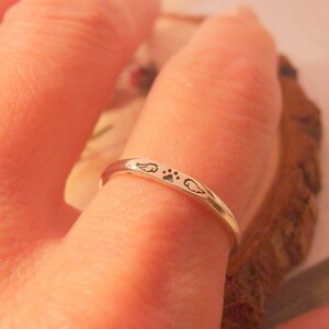 May include: A silver ring with a paw print and two wings engraved on it. The ring is worn on a finger.