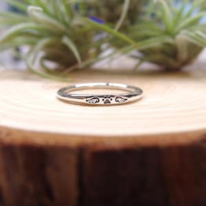 May include: A silver ring with a paw print and wings engraved on it. The ring is on a wooden surface.
