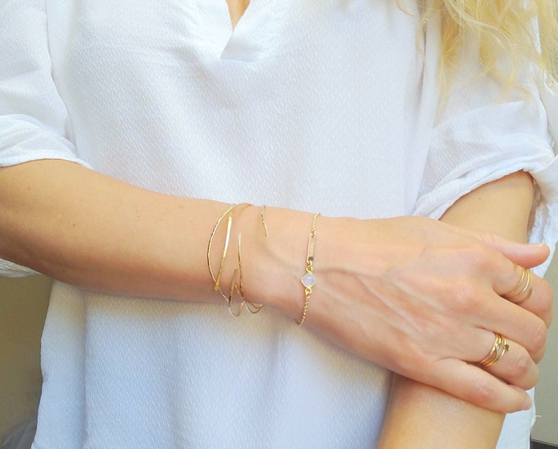 May include: A set of gold bracelets on a person's wrist. The bracelets are thin and delicate, and one has a small white stone charm.