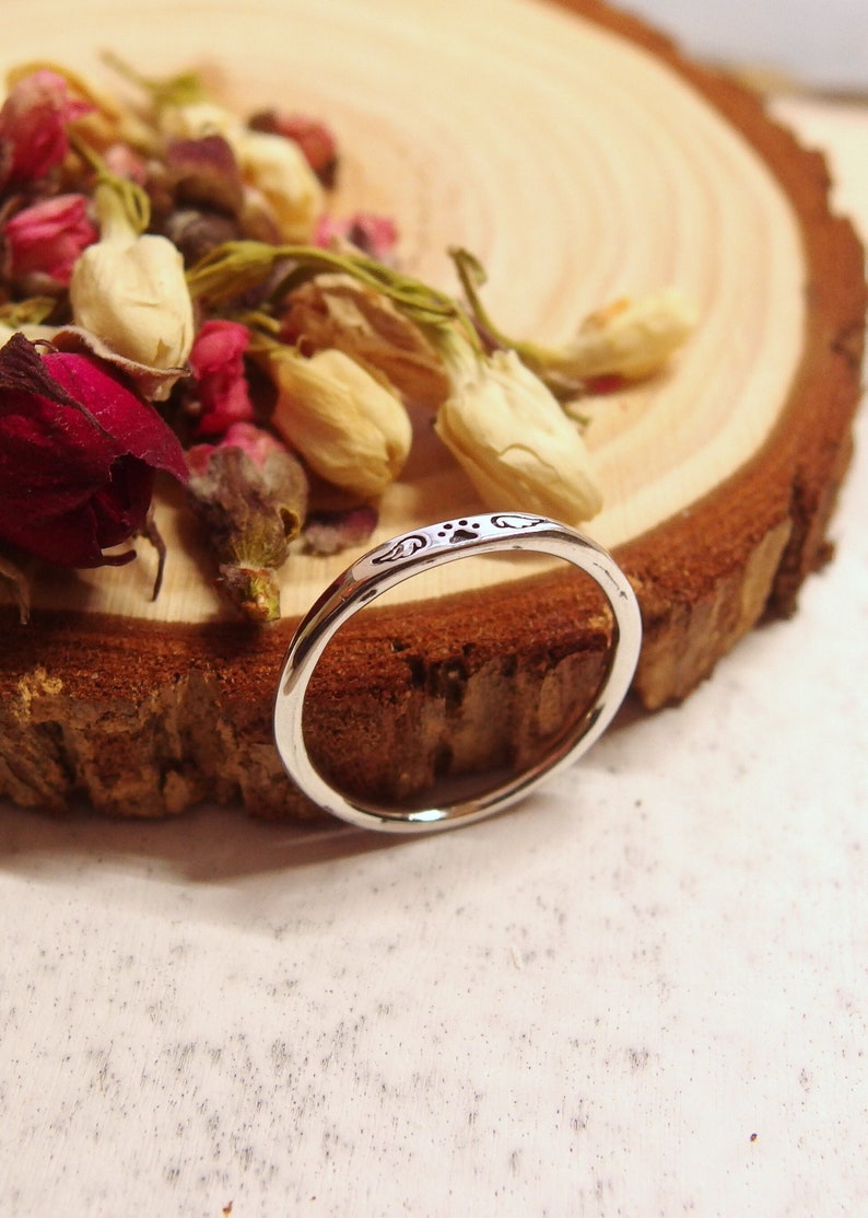 May include: A silver ring with a paw print design. The ring is on a wooden surface with dried flowers.