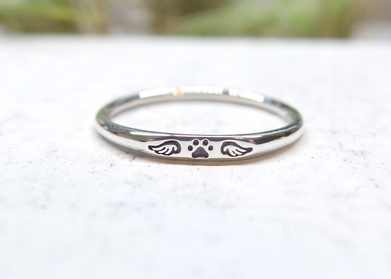 May include: A silver ring with a paw print and wings engraved on the band.