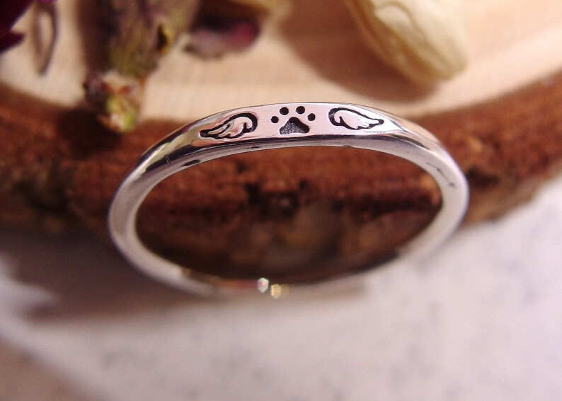 May include: A silver ring with a paw print and angel wings engraved on the band.