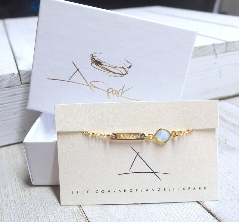 May include: A gold chain bracelet with a small, clear gemstone and a gold charm that says "UNICORN". The bracelet is displayed on a white card with the text "etsy.com/shop/angelicspark".