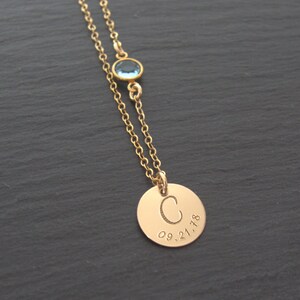 May include: Gold necklace with a round pendant engraved with the letter "C" and the date "09.21.18". A small blue gemstone is attached to the chain above the pendant.