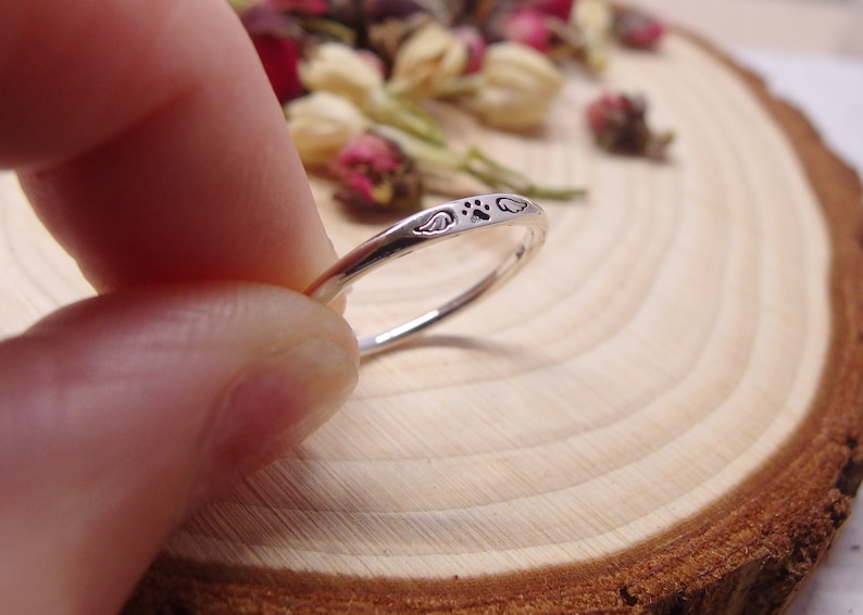 May include: A silver ring with a paw print and two angel wings engraved on the band.