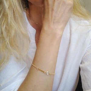 May include: A gold chain bracelet with a small, white, rectangular stone charm. The chain is twisted and has a delicate design.