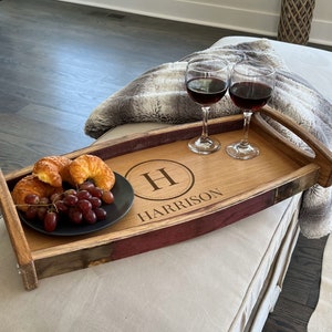 May include: A wooden serving tray made from a reclaimed wine barrel with a personalized monogram and the name "HARRISON" engraved on the surface. The tray has a handle on one side and is filled with snacks and wine glasses.
