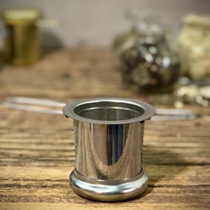 Puede incluir: Un infusor de t&eacute; de acero inoxidable con un filtro de malla fina. El infusor tiene una base redonda y un cuerpo cil&iacute;ndrico.