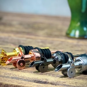 May include: Four bottle pourers in different finishes: gold, copper, black, and silver. Each pourer has a black rubber stopper and a spout for controlled pouring.