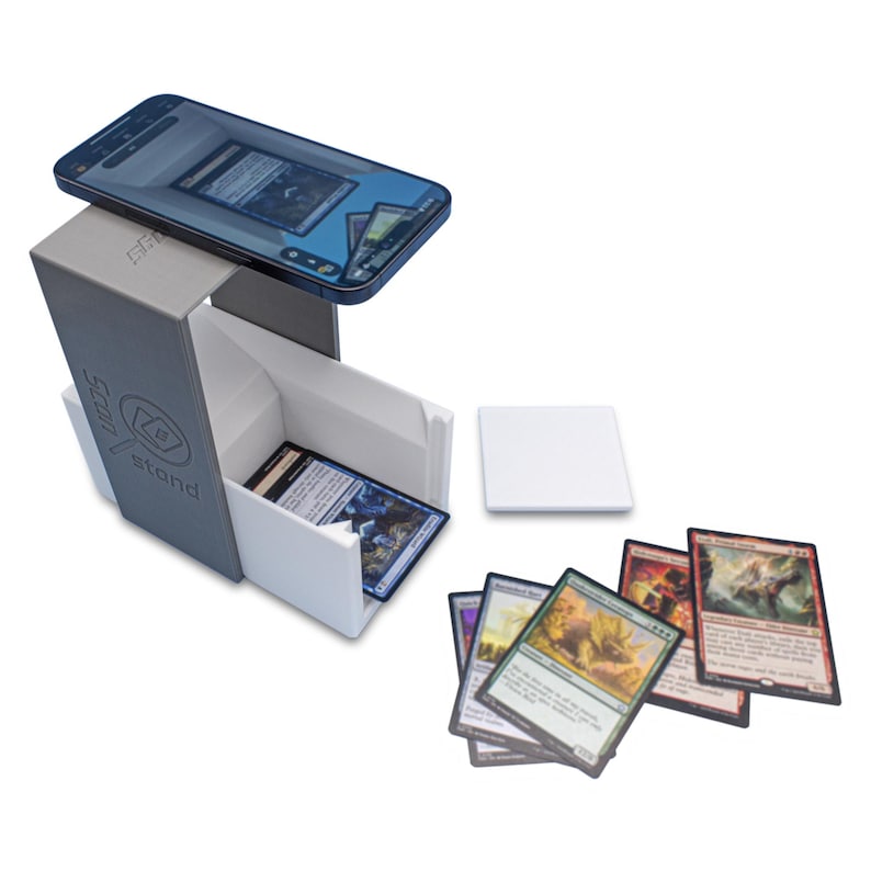 May include: A white and gray card game stand with a phone holder on top. The stand has the word "stand" and the text "dice" printed on it. There are several playing cards scattered around the stand.