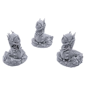 May include: Three gray 3D printed miniature figures of a creature with a segmented body and multiple tentacles. The creature is curled up in a defensive posture, with its tentacles wrapped around its head. The figures are set on a base of textured gray plastic.