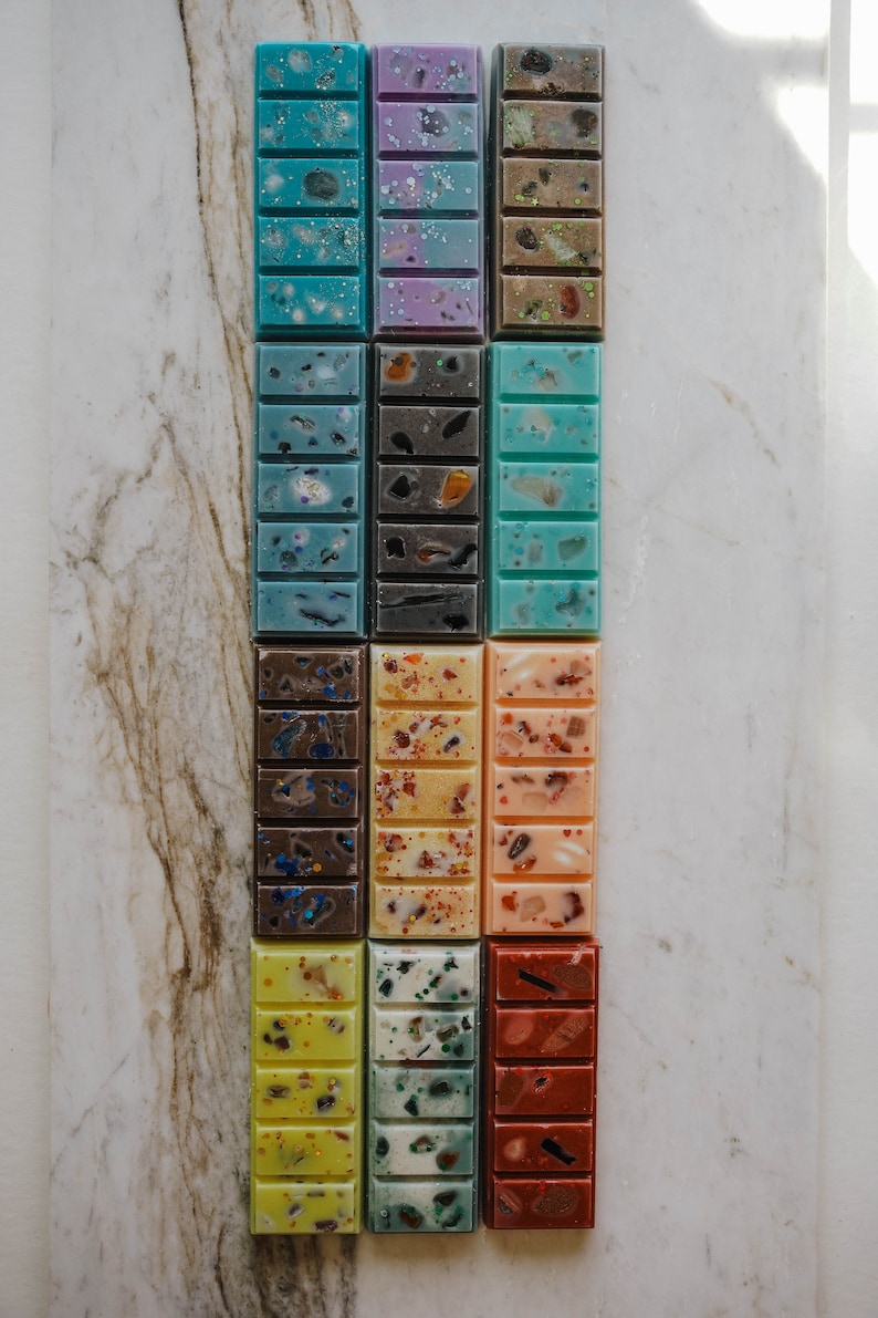 May include: A set of 12 wax melts in various colours and patterns, including blue, green, yellow, orange, brown, and purple. The wax melts are arranged in three rows of four, with each melt having a different design.