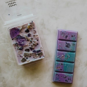 May include: Two wax melts, one in a clear plastic container with purple wax and embedded crystals, and one in a rectangular bar with purple and blue wax and glitter.
