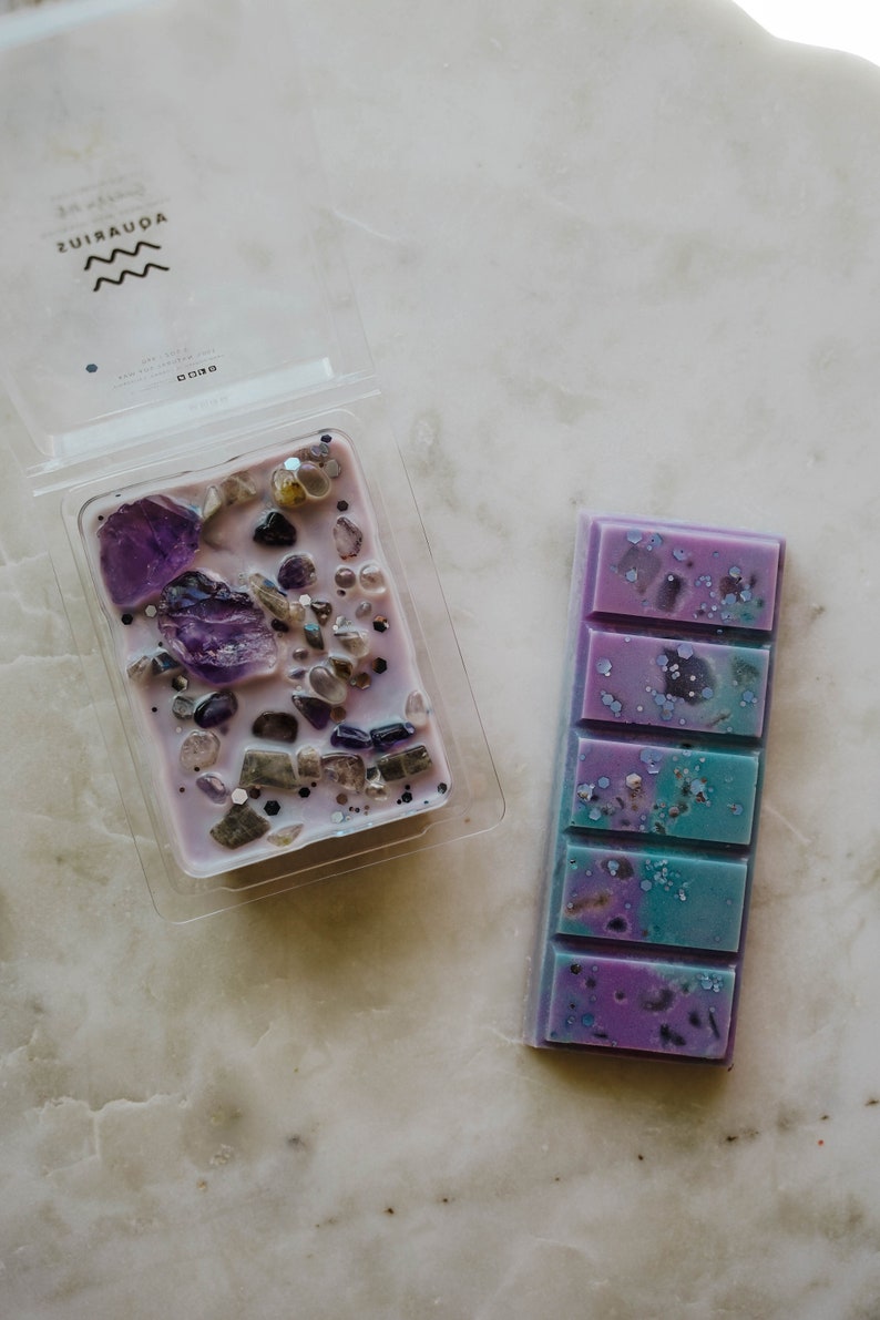 May include: Two wax melts, one in a clear plastic container with purple wax and embedded crystals, and one in a rectangular bar with purple and blue wax and glitter.