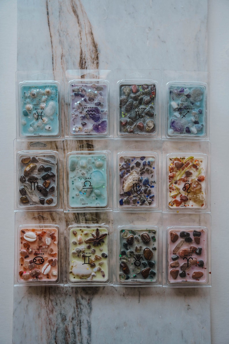 May include: Twelve clear plastic containers with wax melts inside. Each container has a different zodiac sign and a variety of colours and textures. The signs are Pisces, Aquarius, Capricorn, Sagittarius, Scorpio, Libra, Virgo, Leo, Cancer, Gemini, Taurus, and Aries.