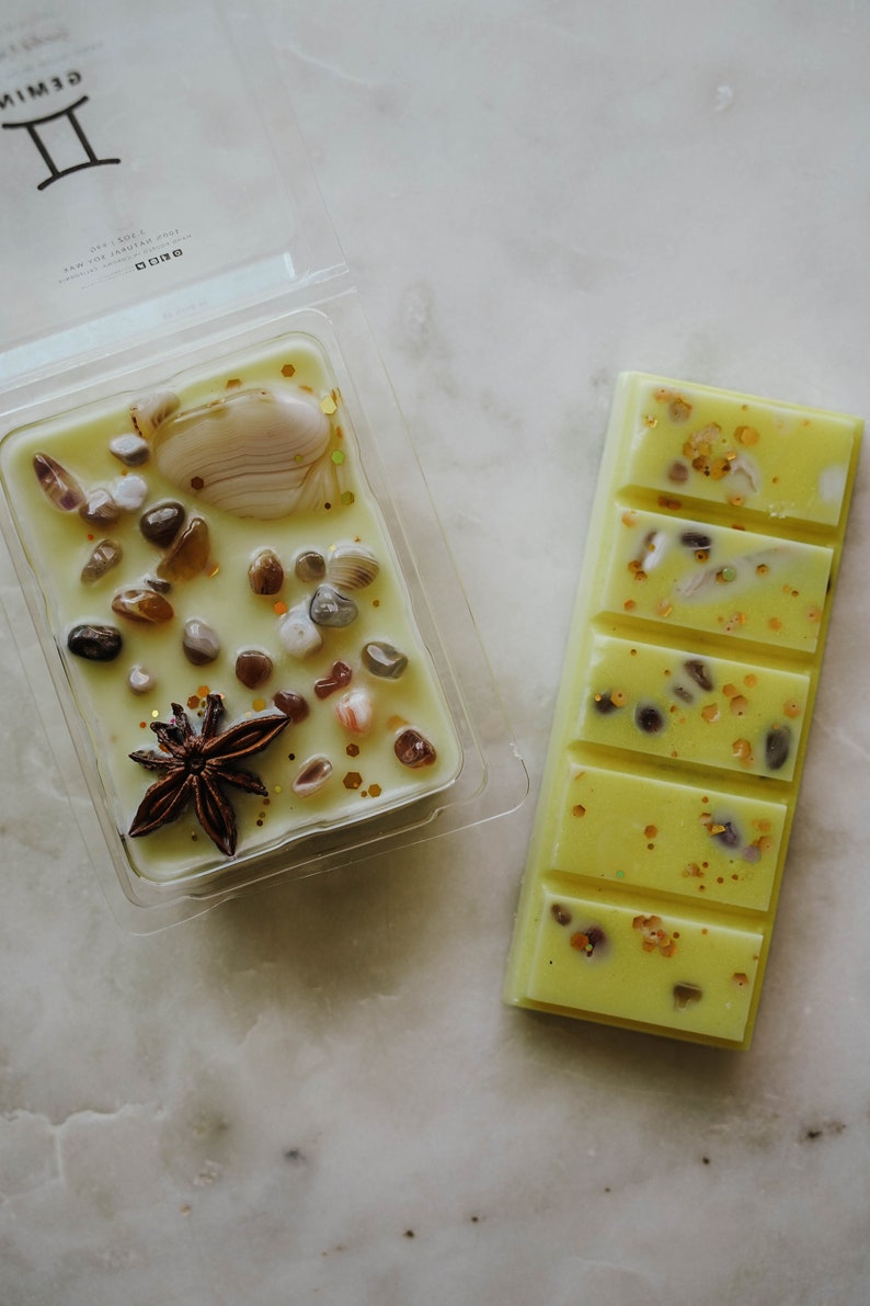 May include: Two wax melts, one in a clear plastic container and one in a bar shape. Both are yellow with embedded glitter and small pieces of seashells. The wax melt in the container also has a star anise.