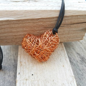 May include: A copper wire heart pendant necklace with a black leather cord. The heart is made of tightly woven copper wire, creating a textured and intricate design.