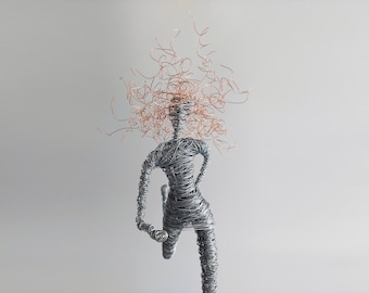 May include: A sculpture of a running figure crafted from silver-toned wire. The figure features a dynamic pose with one leg forward and arms bent. The head is topped with a dense, chaotic mass of thin, curly copper-colored wire strands.