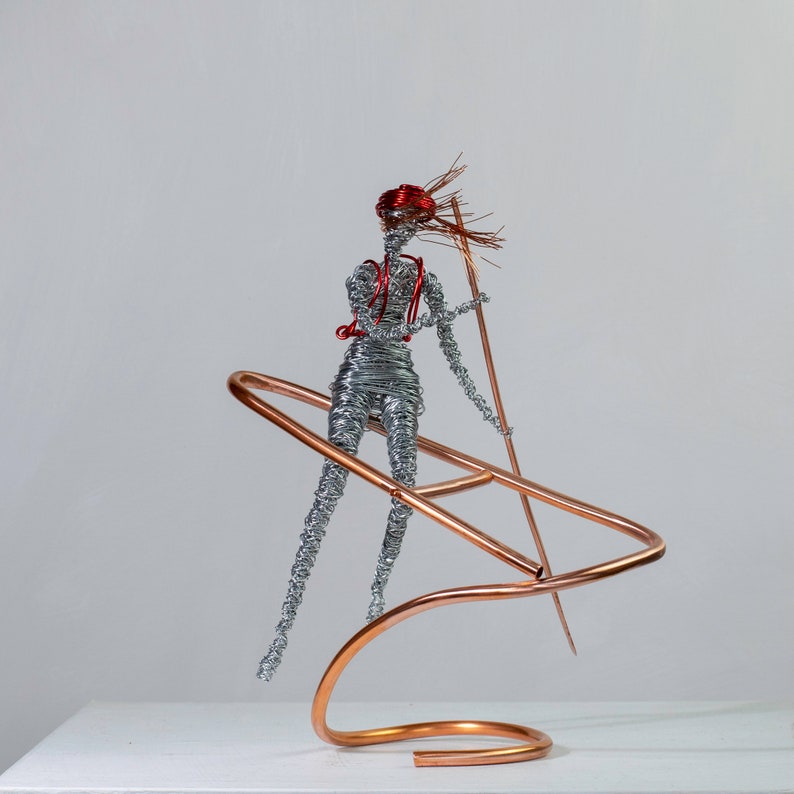 Handmade female rafter wire sculpture holding a paddle, with red hair, a copper wire raft and aluminum wire details.