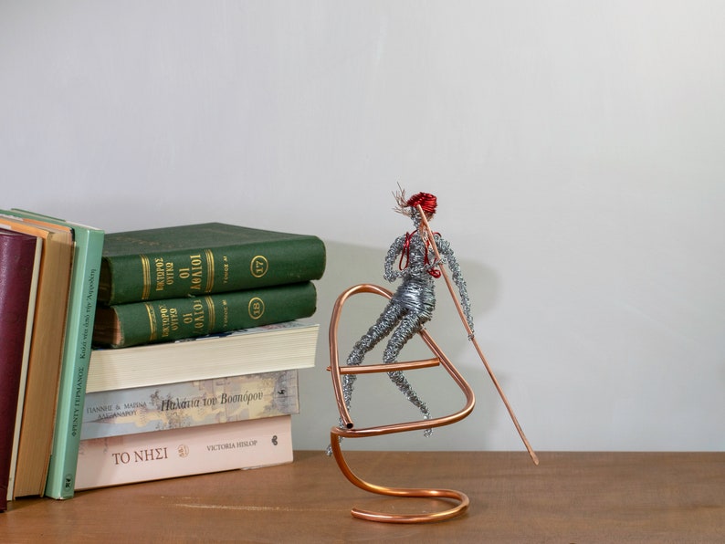 Handmade female rafter wire sculpture holding a paddle, with red hair, a copper wire raft and aluminum wire details.