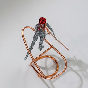Handmade female rafter wire sculpture holding a paddle, with red hair, a copper wire raft and aluminum wire details.