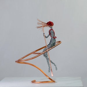Handmade female rafter wire sculpture holding a paddle, with red hair, a copper wire raft and aluminum wire details.