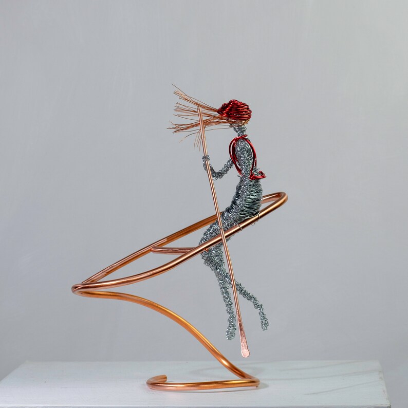 Handmade female rafter wire sculpture holding a paddle, with red hair, a copper wire raft and aluminum wire details.