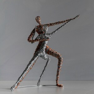 May include: A sculpture of two figures dancing, constructed from intertwined silver and copper-colored wire. The figures are captured in a dynamic pose with one arm extended outward, showcasing a textured, layered metal design throughout.