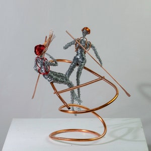 Two handmade wire rafter sculptures with paddles on a copper wire raft, showing red and orange aluminum wire details.