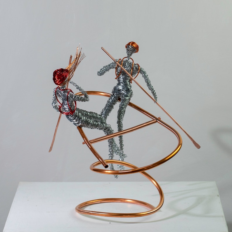 Two handmade wire rafter sculptures with paddles on a copper wire raft, showing red and orange aluminum wire details.