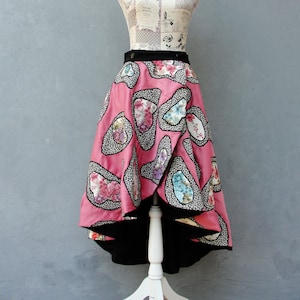 May include: A pink high-low skirt with a black lining and a floral pattern. The skirt is made of fabric with a textured surface and is displayed on a white mannequin.