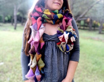 May include: A woman wearing a gray dress with a colorful knitted scarf. The scarf is made of different colored yarn and has a ruffled texture.