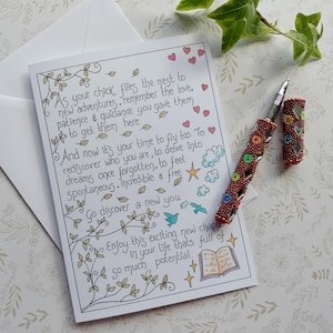 May include: A greeting card with handwritten text and a decorative pen. The card has a floral border and the text reads, "As your chick flies the nest...Go discover a new you." The pen is red with colorful beadwork.