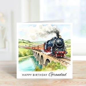 May include: A square greeting card featuring a watercolor illustration of a black steam locomotive pulling red passenger cars across a stone arch bridge over a river. The text at the bottom reads HAPPY BIRTHDAY Grandad in black lettering.