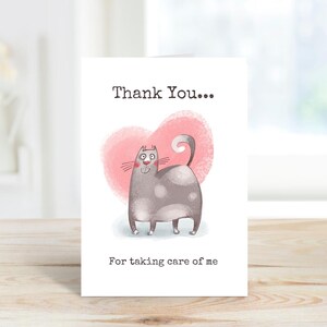 Könnte beinhalten: Eine weiße Grußkarte mit dem Text "Thank You... For taking care of me." Die Karte zeigt eine Cartoon-Illustration einer grauen Katze mit weißen Flecken, vor einem rosa herzförmigen Hintergrund.