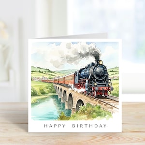 May include: A square greeting card featuring a watercolor illustration of a black steam locomotive pulling red passenger cars across a stone arch bridge over a river. The text HAPPY BIRTHDAY is printed in black capital letters at the bottom.