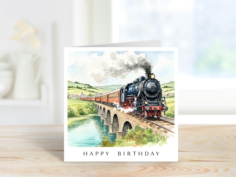 May include: A square greeting card featuring a watercolor illustration of a black steam locomotive pulling red passenger cars across a stone arch bridge over a river. The text HAPPY BIRTHDAY is printed in black capital letters at the bottom.